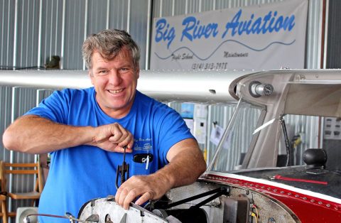 Main smiling at camera while making repair on plane engine