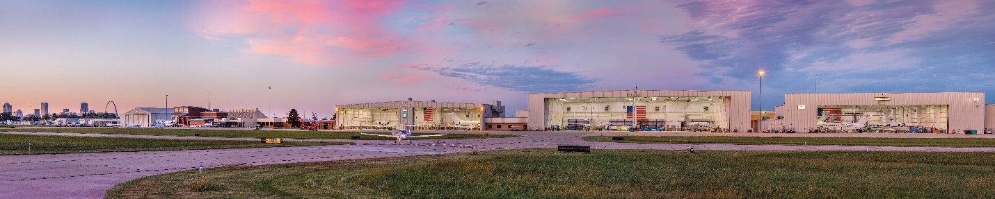 A panoramic photo of hangers and planes at the St. Louis Downtown Airport with the St. Louis skyline in the background.